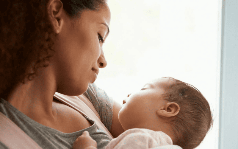 Mãe segurando seu bebê no colo com carinho, representando o vínculo afetivo e os primeiros cuidados maternos.