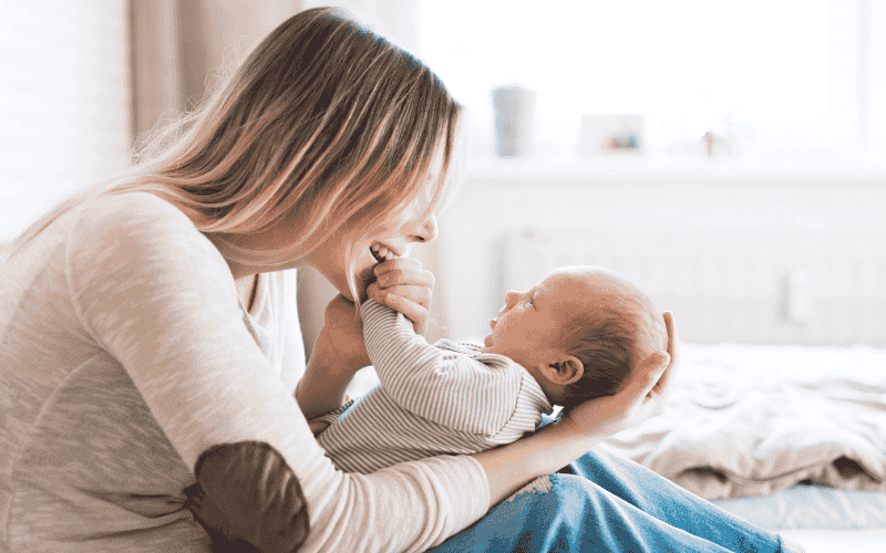 Mãe segurando seu bebê no colo com carinho, representando o vínculo afetivo e os primeiros cuidados maternos.